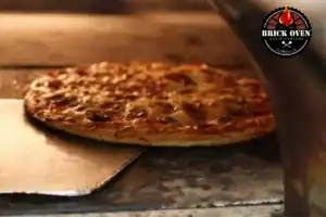 Close-up of a pizza being pulled out of a brick oven on a metal tray