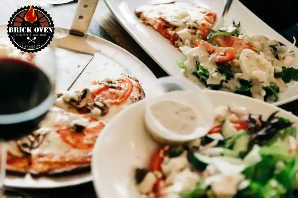 A pizza and side salad with dressing served on a plate, with a glass of wine in the background.