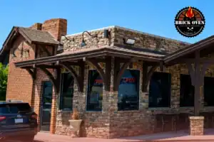 Brick oven pizzeria storefront with outdoor seating.